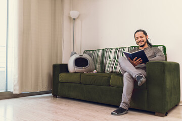 Young man reading a book at home sitting on the couch in the living room