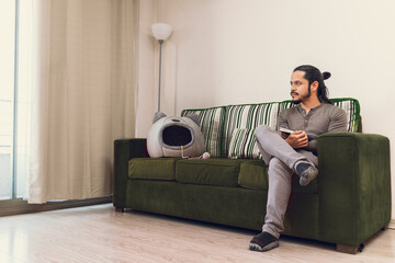 Young man reading a book at home sitting on the couch in the living room