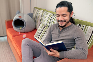 Young man reading a book at home sitting on the couch in the living room