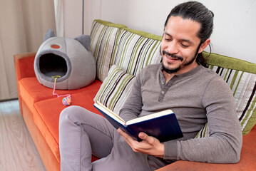 Young man reading a book at home sitting on the couch in the living room