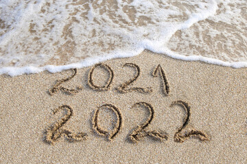 2021, 2022 years written on sandy beach sea. Wave washes away 2021.