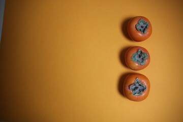 Persimmons laying in row with copy space on orange background