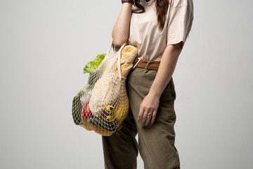 Portrait of smiling young woman in oversize t-shirt holding reusable string bag with groceries....