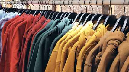 Obraz premium Bright colorful sweatshirts hanging at a fashion store. Closeup of multi-colored yellow, red, pink, geen sweatshirts hang in a row on a hanger at clothes shop in the shopping mall.