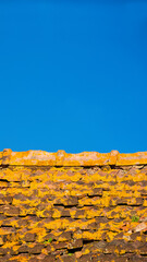 Old and ruined roof tiles with yellow lichens, blue sky and copy space above