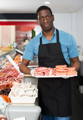 Professional positive adult butcher arranging meat products in display case of butcher shop