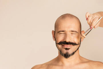 Cosmetics for men's makeup. Cosmetics for the face. Woman's hands with a brush. Happy bald and bearded man..
