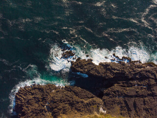 Aerial view. Rocky ocean shore and dark turquoise water with white foam waves. Minimalism. There are no people in the photo. Beautiful nature. Swimming, fishing, trade, environmental protection.