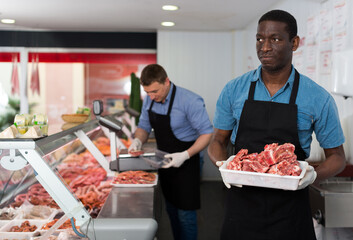Fototapeta na wymiar Skillful butcher with colleague working behind counter in butchery