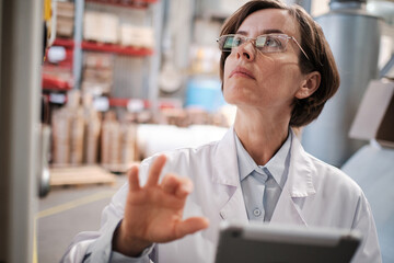 Woman with tablet working with industrial machine at factory