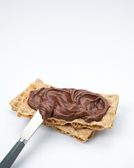 Slices of rye cracker bread with healthy chocolate hazelnut spread, with knife on white background, space for text.