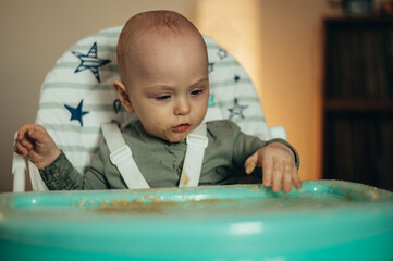 Baby eating with a face stained in food while in a child's dining chair