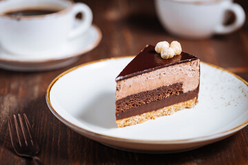 Chocolate hazelnut cake with five layers of biscuit and cream with chocolate glazing on top and whole nuts from Piemont. Served and decorated with coffee in background