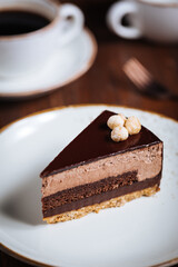 Chocolate hazelnut cake with five layers of biscuit and cream with chocolate glazing on top and whole nuts from Piemont. Served and decorated with coffee in background