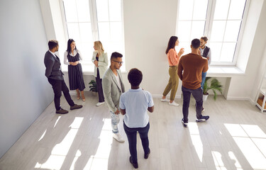 Diverse people talking in groups during a meeting. High angle shot of different young community members or company employees standing in a modern office room, discussing something, sharing opinions