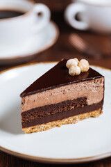 Chocolate hazelnut cake with five layers of biscuit and cream with chocolate glazing on top and whole nuts from Piemont. Served and decorated with coffee in background