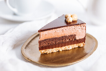 Chocolate hazelnut cake with five layers of biscuit and cream with chocolate glazing on top and whole nuts from Piemont. Served and decorated with coffee in background