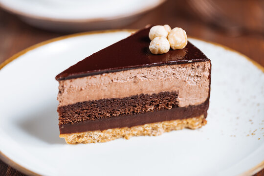 Chocolate hazelnut cake with five layers of biscuit and cream with chocolate glazing on top and whole nuts from Piemont. Served and decorated with coffee in background