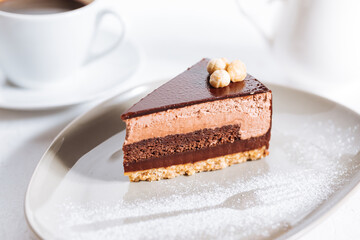 Chocolate hazelnut cake with five layers of biscuit and cream with chocolate glazing on top and whole nuts from Piemont. Served and decorated with coffee in background