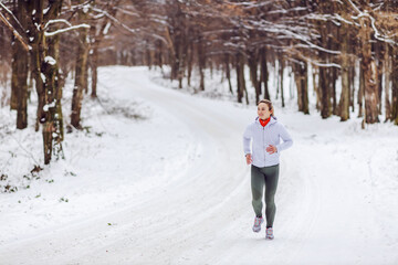 Fit sportswoman running in nature on a snowy winter day. Cold weather, snow, healthy life, fitness, nature