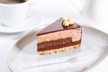 Chocolate hazelnut cake with five layers of biscuit and cream with chocolate glazing on top and whole nuts from Piemont. Served and decorated with coffee in background