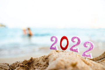 Figures 2022 against background of coastal waves by ocean or sea with caramel cane. Travel during quarantine on New Year's Eve against the background of people swimming in the sea