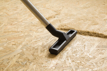 Black nozzle of professional vacuum cleaner vacuuming sawdust from osb board floor. Closeup....