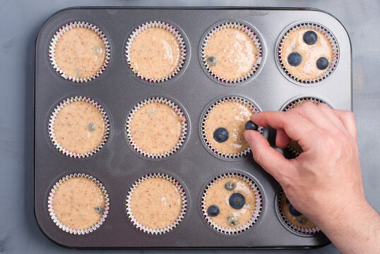 Person adding blueberries in muffins batter in form for cooking