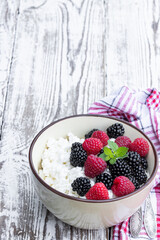 Cottage cheese with fresh raspberry and blackberry in ceramic bowl on white wooden table