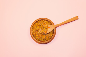 Bee leg. A pile of bee pollen grains in a wooden bowl with a wooden spoon.