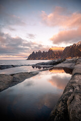 Tugeneset viewpoint in Senja, Norway at sunset with reflections of the mountains and the landscape in the calm water among the cliffs