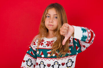 little kid girl wearing knitted sweater christmas over red background looking unhappy and angry...