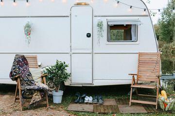 trailer of mobile home or recreational vehicle stands on shore of pond in camping in autumn near table set, concept of family local travel in native country on caravan or camper van and camping life