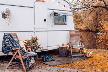 trailer of mobile home or recreational vehicle stands on shore of pond in camping in autumn near...