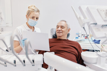 Obraz premium Woman doctor dentist works with an elderly man in a dental chair treats teeth and shows x-rays