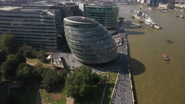 people walking on waterfront near futuristic buildings of City hall. Tilt up reveal of cityscape. London, UK