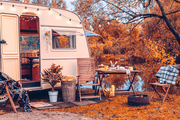 trailer of mobile home or recreational vehicle stands on shore of pond in camping in autumn near...