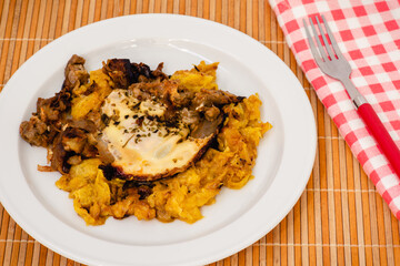 Plato de berenjenas con naranja y miel, un huevo frito encima, una servilleta a cuadros y un tenedor rojo
