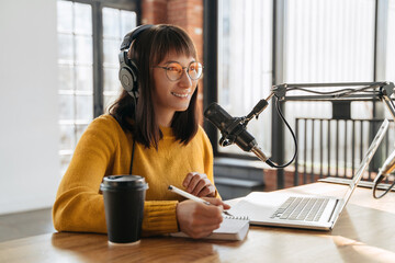 Podcasting and blogging. Young smiling woman broadcasting an audio podcast for her online show in...