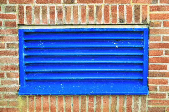 Blue ventilation duct in an industrial building.
Air intake and outtake of the ventilation system in an industrial building. Blue grille in a brick wall.