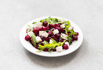 Beetroot, cottage cheese and arugula salad with white and black sesame seeds on a plate on a light gray background