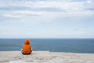 A man sits in the frame, facing the sea. Minimalistic shot of man and the sea. Bright clothes, calm sea. Time alone. PRogulka by the sea