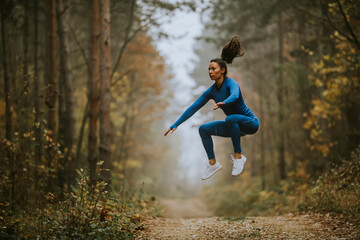 Young woman taking high jump on the forest trail at autumn