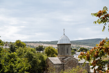 Ancient single-domed temple. Historical building in the middle of the landscape. Church and service, cross on the dome. Around the temple there are green trees