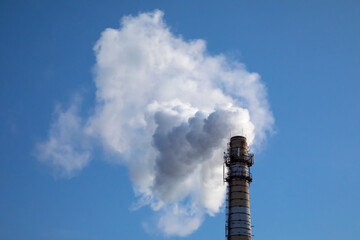 White steam or smoke is blown in the wind against the blue sky. Air pollution in city
