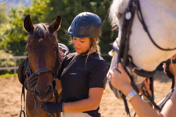 Obraz premium Posing of two young Caucasian girls riders with their white and brown horses on a horse, dressed in black with safety caps