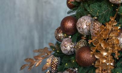 Decorated Christmas tree on grey background. Bronze and golden christmas ornaments fir tree brunch close up. Shallow focus. Winter holidays wallpaper concept. Copy space