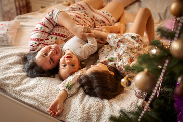 mom and two children lie on the bed at home in beautiful Christmas pajamas next to the Christmas tree. 