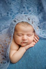 Sleeping newborn infant baby on a blue background covered by blanket. A few days from birth. Kid is holding hands under the cheek.