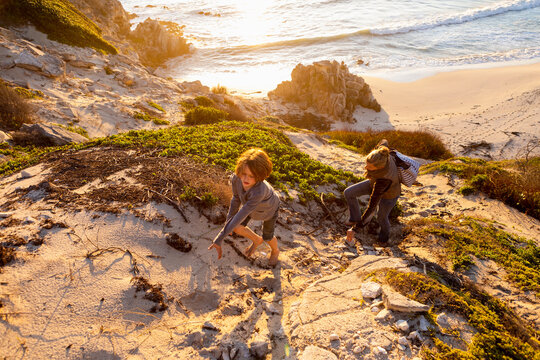 Young boy and mature woman climbing up a cliff path at sunset. 
